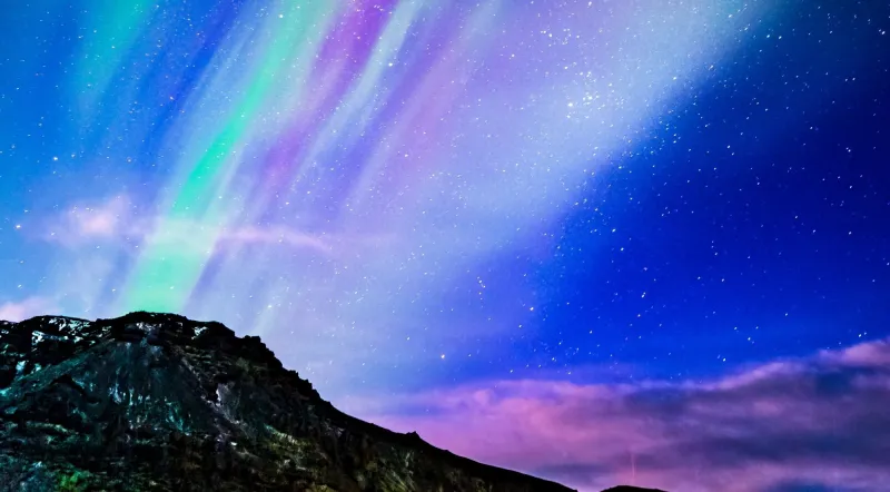 Faint aurora and starry sky above a dark mountain ridge in southeast Iceland